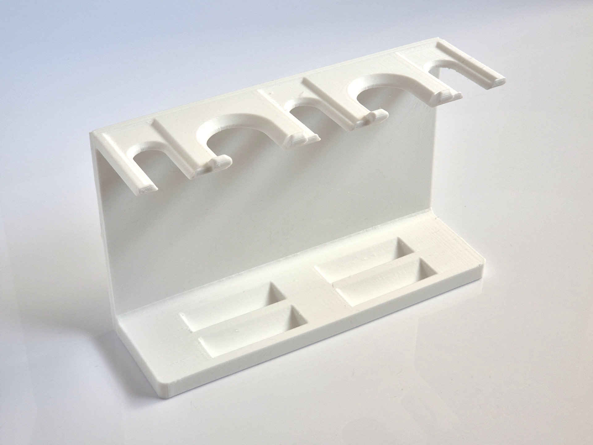 White upright shaving rack shot at an angle on white, with three hooked cradles and a further hook along the top rail and two shallow rectangular trays in the base.