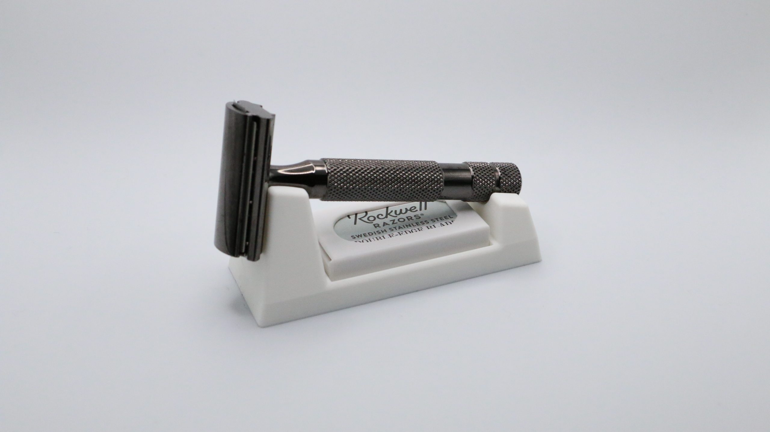 Closer studio view of the ivory wedge from the end, razor head pointing up and handle lying in the channel, blade box in the front slot.