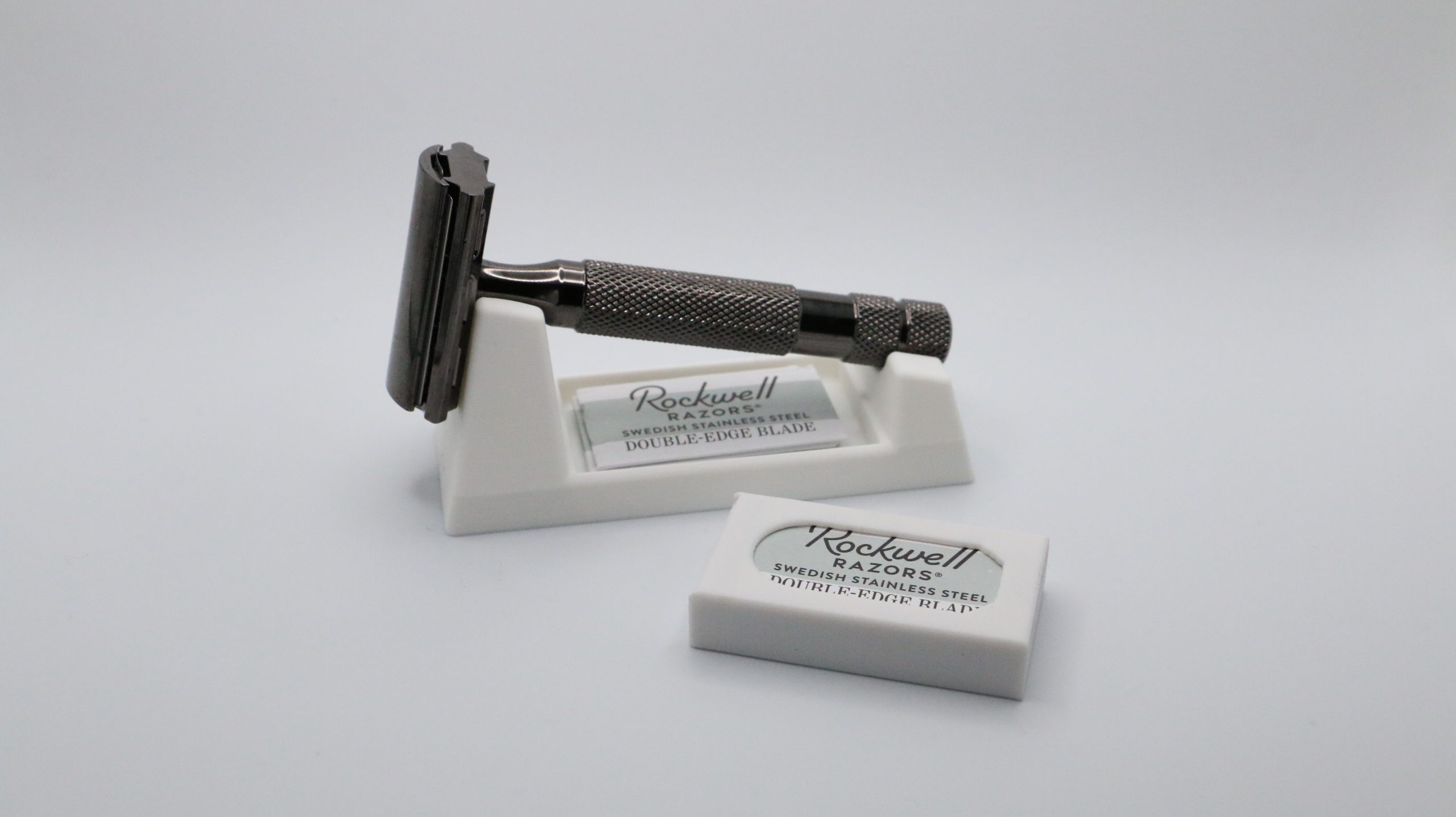 Ivory 3D printed wedge rest on white with a dark safety razor lying in the cradle, a Rockwell Razors blade box pushed into the front slot and a second box lying beside it.