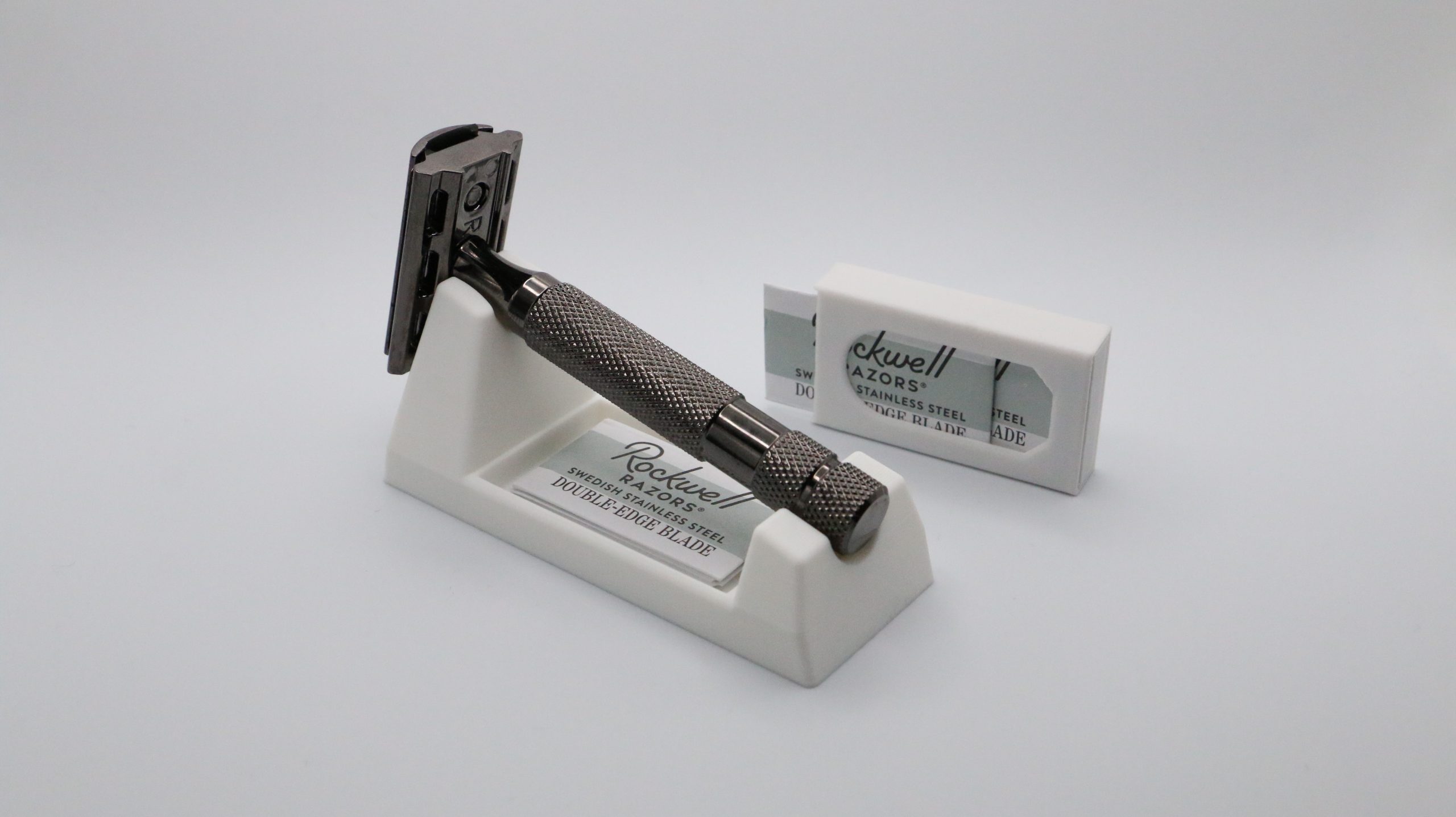 The ivory rest holding a knurled safety razor, a Rockwell Razors blade packet standing upright behind the stand on a plain white surface.