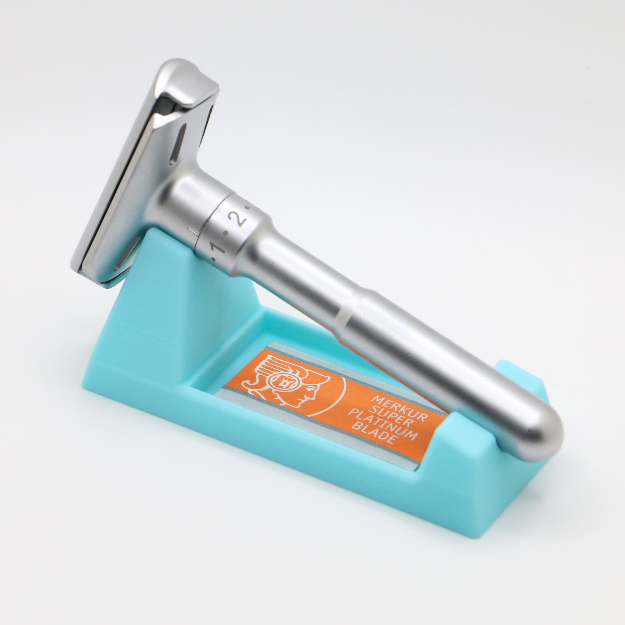 Close three quarter view of the turquoise wedge and adjustable razor, orange blade packet in the tray, showing the dial numbers on the razor handle.