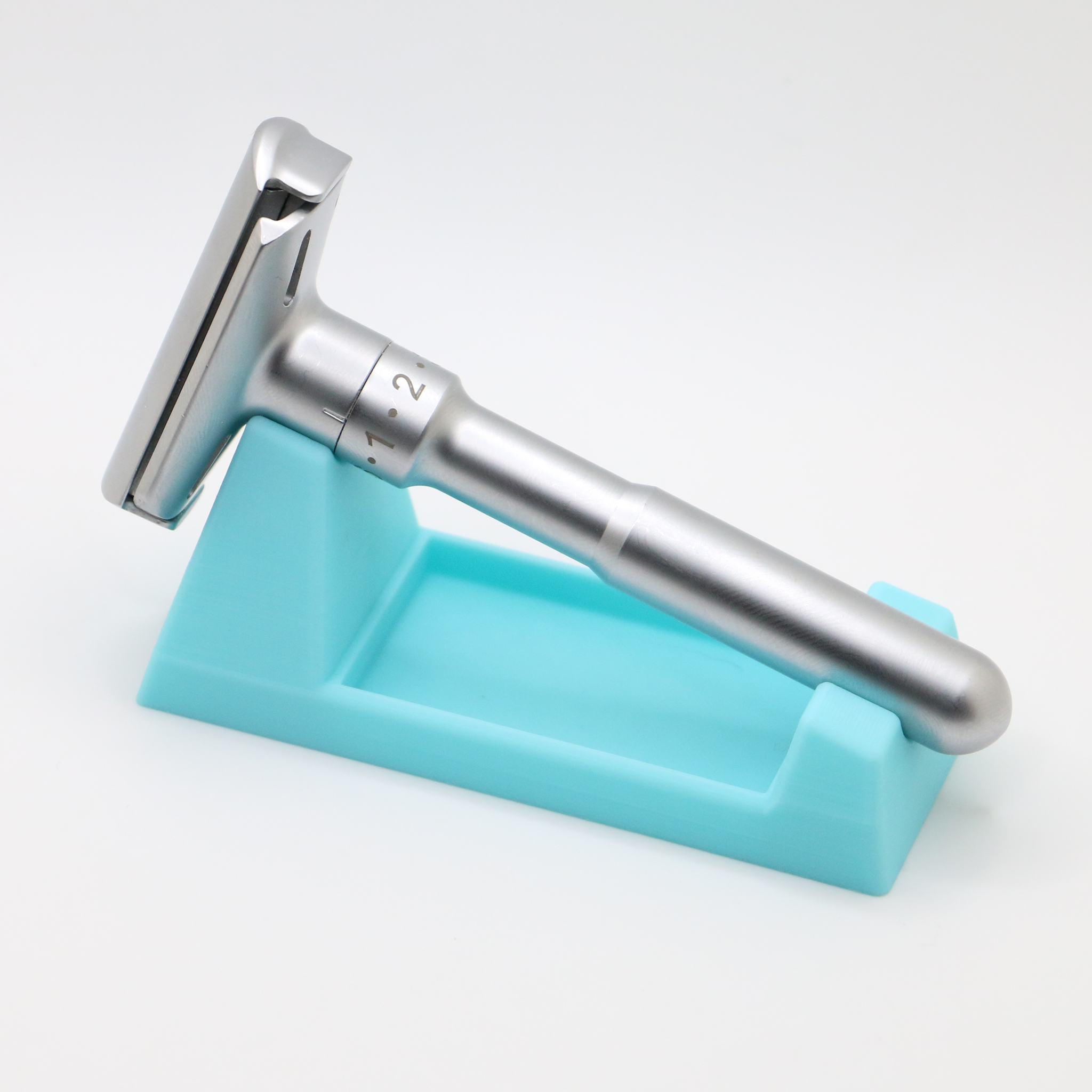 Three quarter view of the turquoise wedge with the adjustable razor resting along it, head to the left, the dial numbers 1 and 2 visible on the handle.