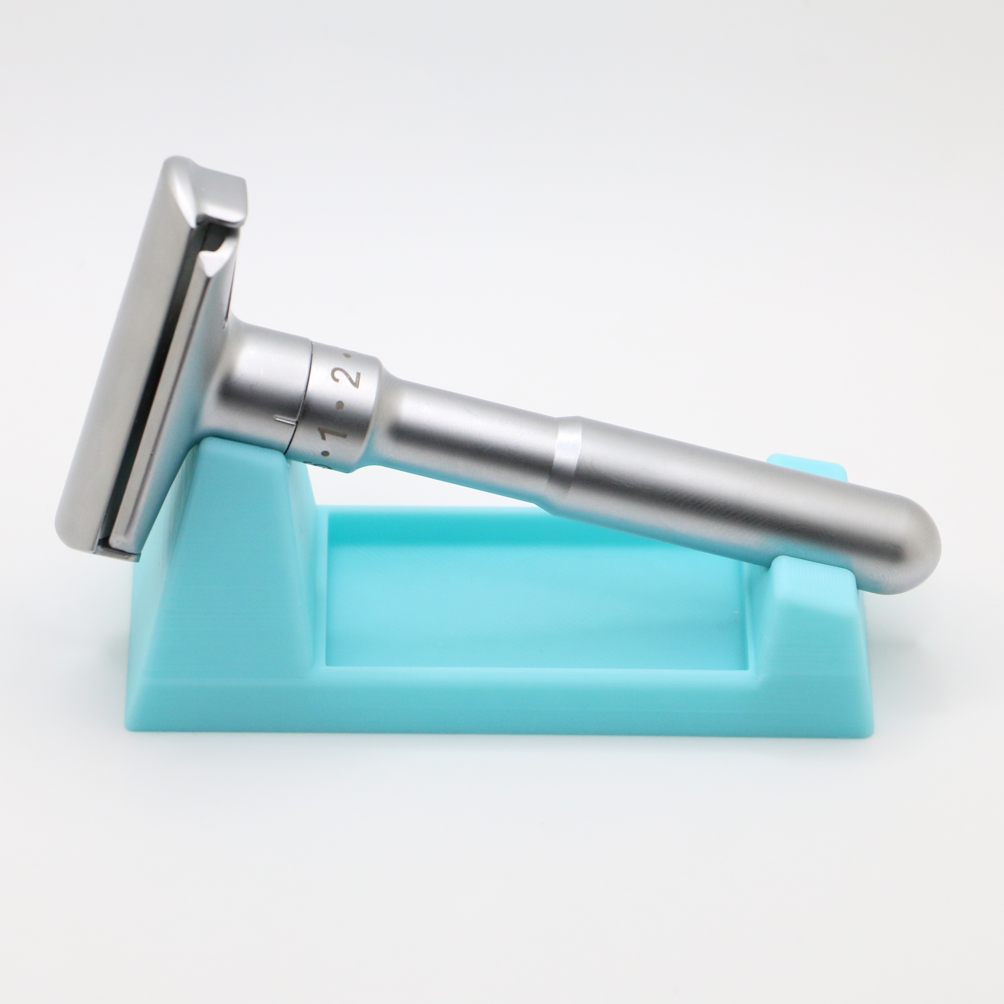 Side profile of the stand and razor, showing the low wedge shape, the raised rear saddle and the long open trough beneath the handle.