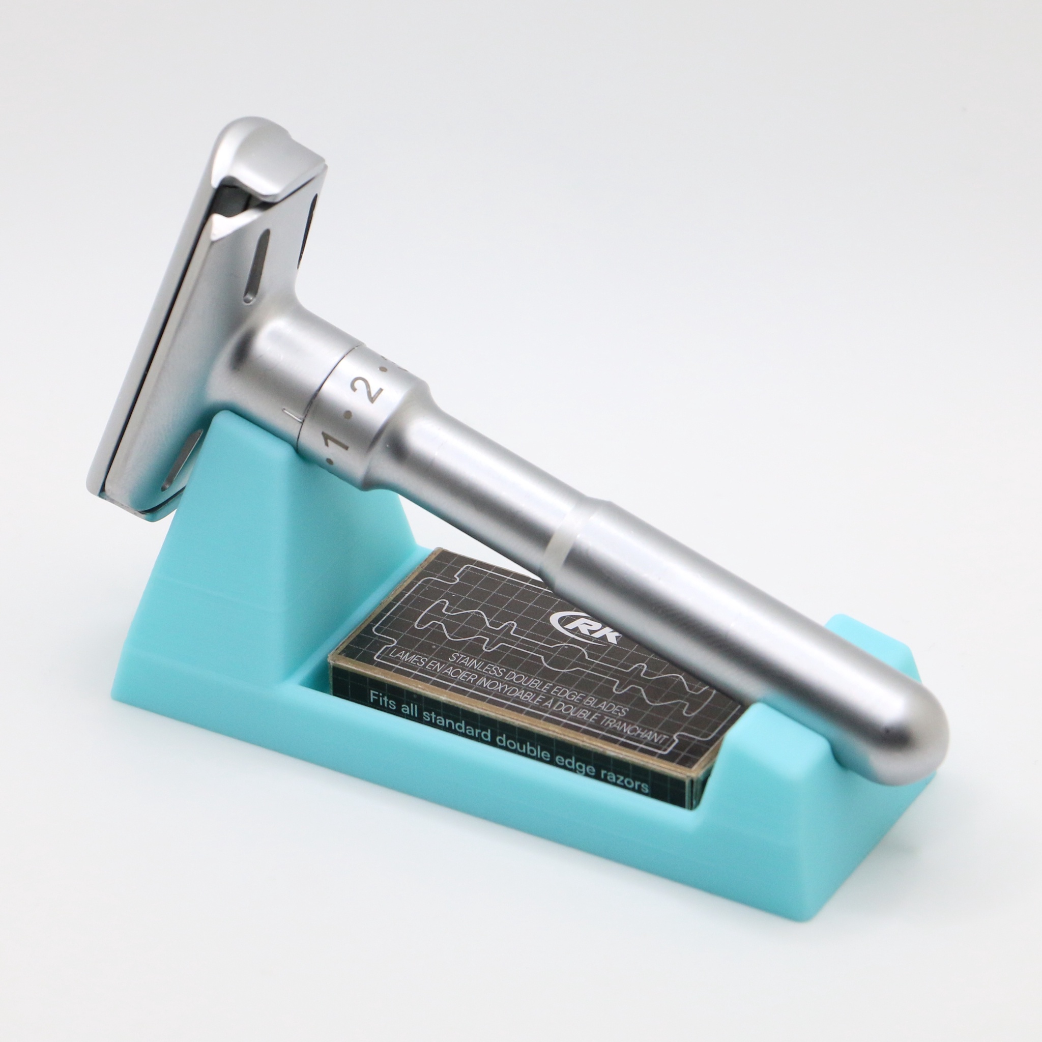 The razor on the turquoise stand with a dark blade carton in the trough, its edge printed fits all standard double edge razors.