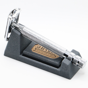 Dark grey speckled granite look 3D printed wedge stand on white, holding a chrome safety razor with a spiral textured handle, with a gold oval maker sticker in the tray.