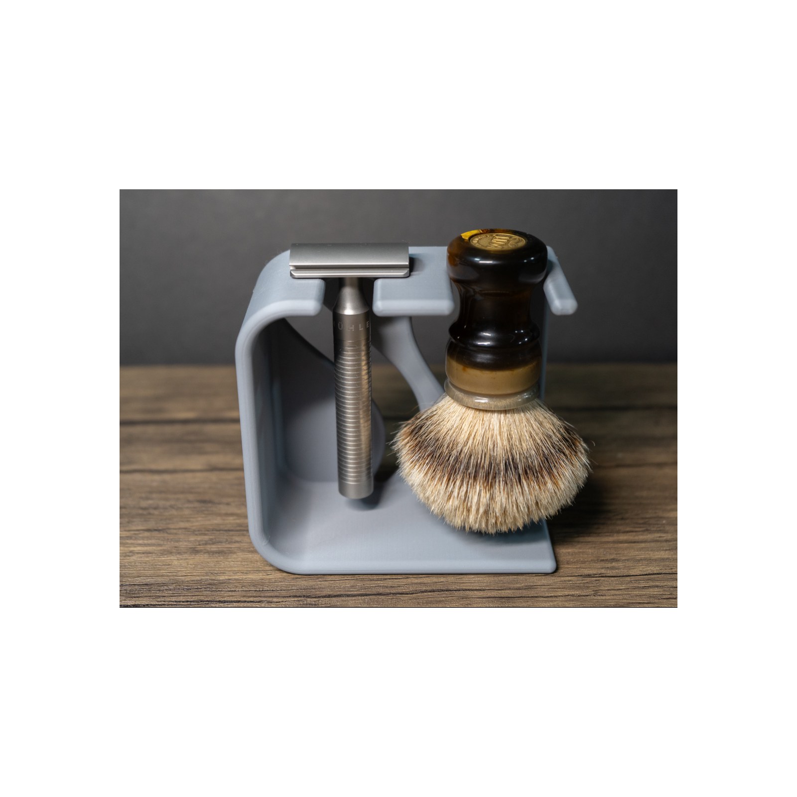 Slightly angled letterboxed view of the loaded stand, showing the flat foot, the smooth matte grey finish and the brush bristles and razor head sitting side by side.