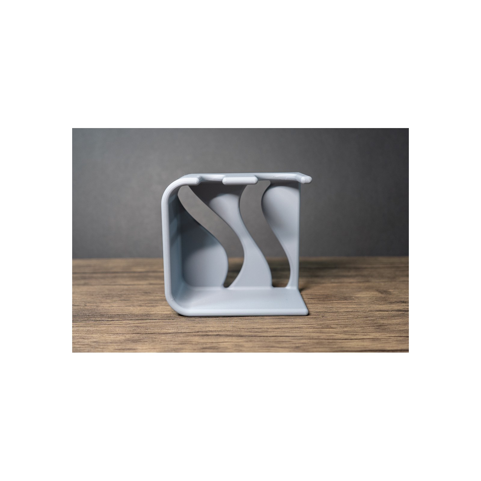 Side profile of the empty holder on wood, the wave shaped inner panels reading as two ribbons running from the back down to the flat base.