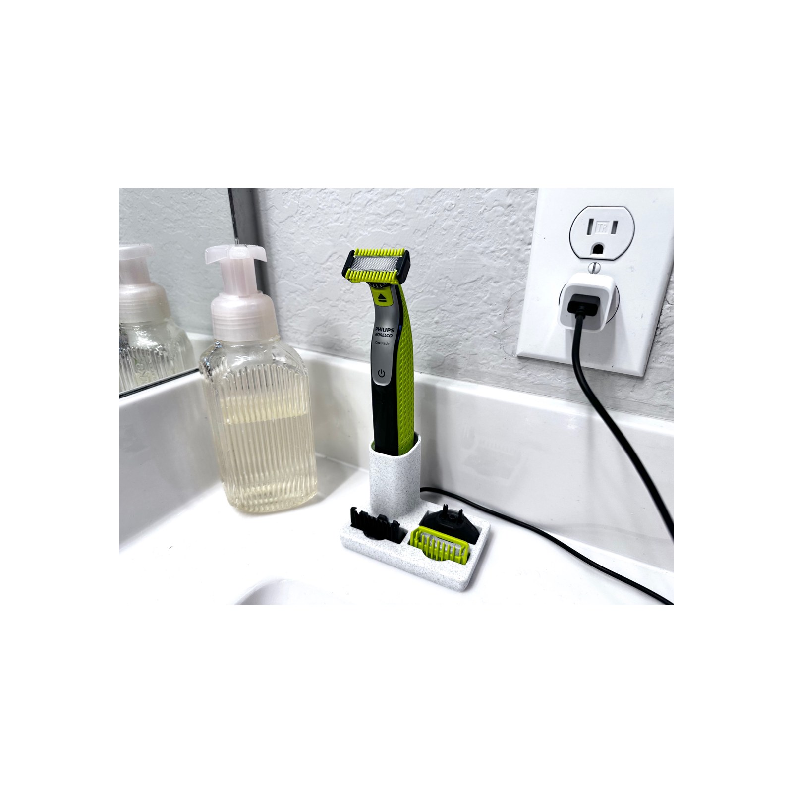 Angled view of the dock at the corner of the basin, trimmer upright in the cup, two comb guards in the tray, cable trailing to the outlet on the right.